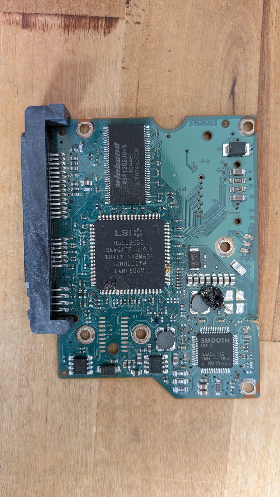 Full view of the Seagate PCB, showing the LSI controller chip, a Winbond DRAM chip, the SMOOTH motor driver, and a cracked, gouged component near the SATA connector