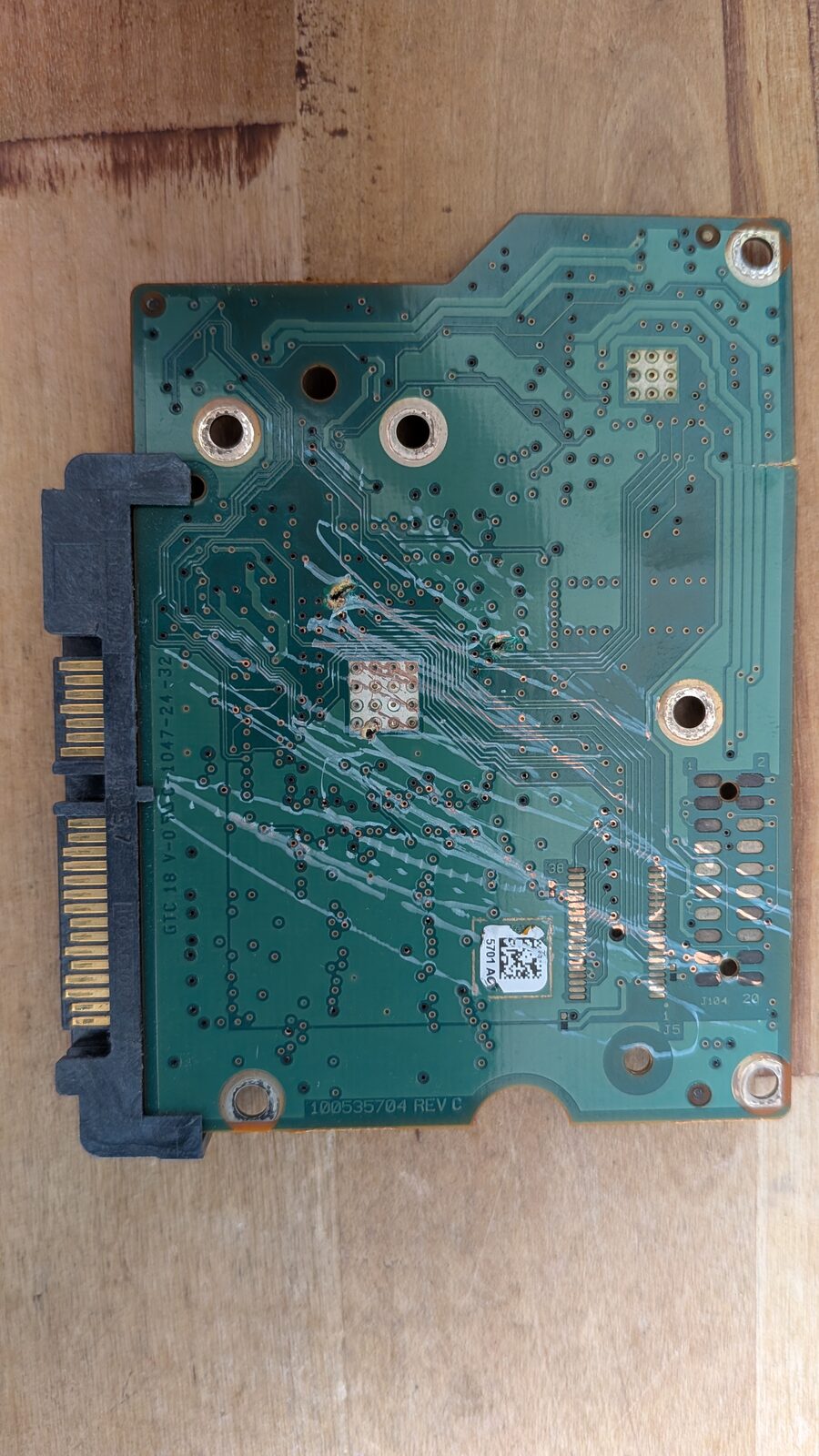 Rear side of the PCB, visibly cracked with two puncture holes gouged through the board down to bare copper